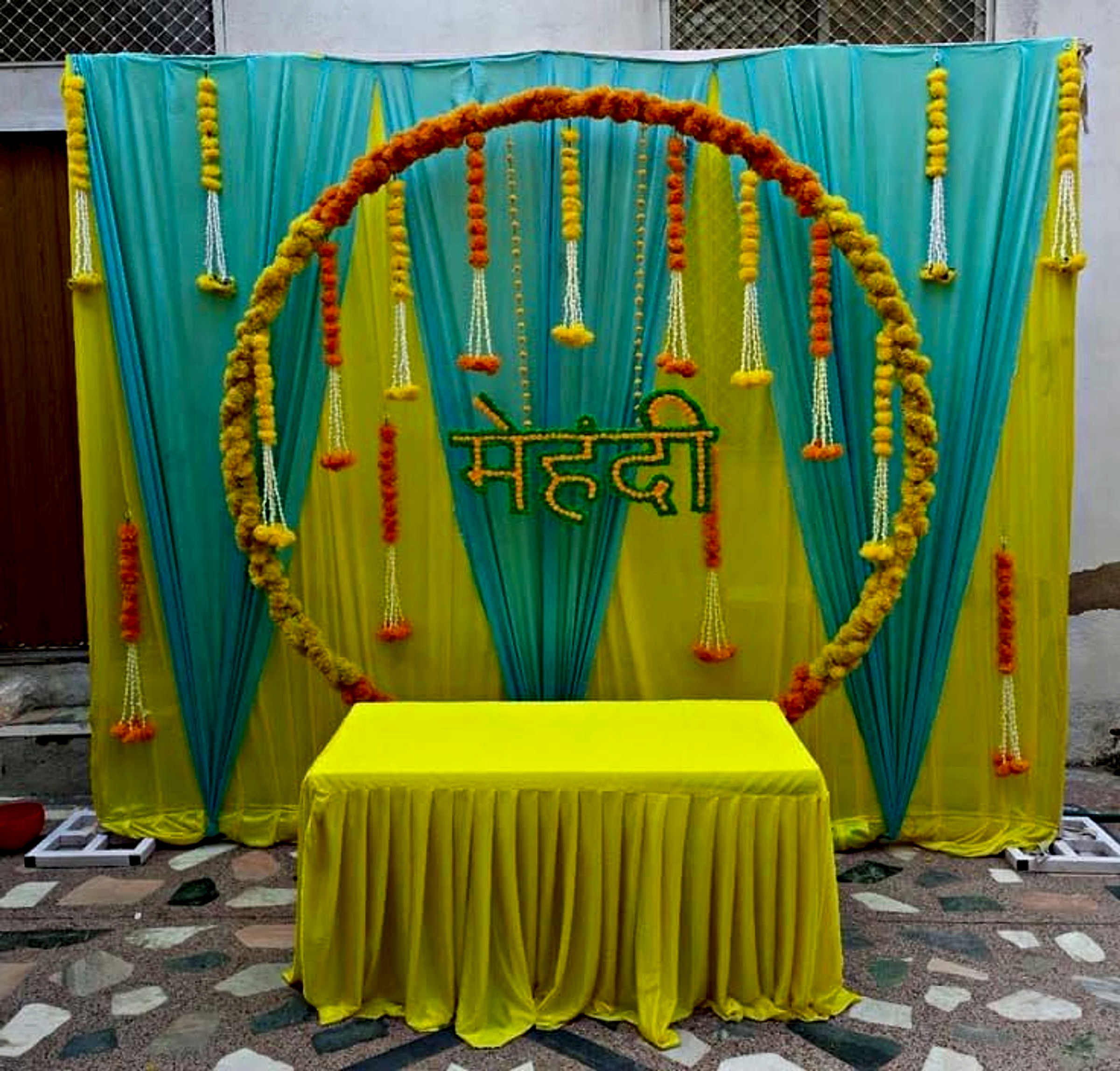 Traditional Mehndi Event Decor In Yellow And Turquoise With Floral Ring Backdrop